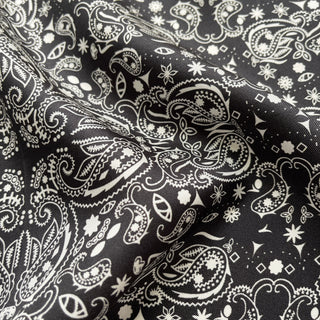 Close-up of black silk scarf with intricate white paisley pattern showing luxurious fabric texture and delicate hand-rolled edges