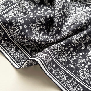 Black silk scarf with white paisley pattern, featuring elegant hand-rolled edges and intricate floral motifs on luxurious twill fabric.