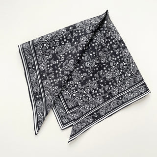 Square black silk scarf with white paisley pattern and hand-rolled edges, elegantly folded showing intricate design and border detail.