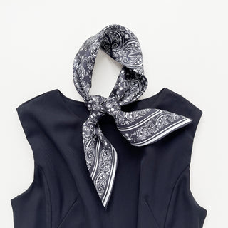 Black silk scarf with elegant white paisley pattern tied in a stylish knot, displayed on a black garment against white background