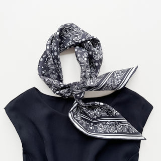 Black silk scarf with white paisley pattern tied elegantly, featuring hand-rolled edges and intricate design displayed on a navy garment