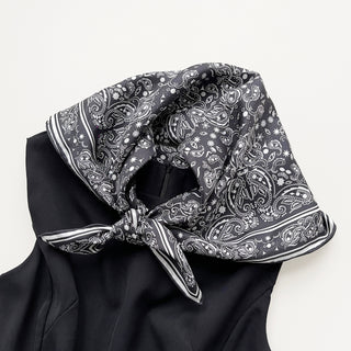 Black silk scarf with white paisley pattern tied elegantly around collar, featuring hand-rolled edges and classic border design