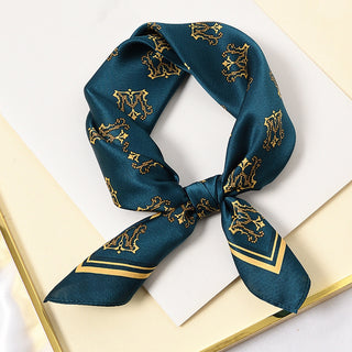 Teal blue silk square scarf with gold crown pattern, tied in a loose knot displaying its luxurious sheen and elegant royal design