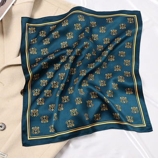 Teal blue silk scarf with repeating golden crown pattern and yellow border, elegantly draped over a beige jacket