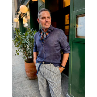 Man wearing a blue patterned silk neckerchief with a navy linen shirt and striped tailored trousers, showcasing timeless men's smart casual style.