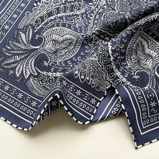 Navy silk scarf featuring intricate white paisley patterns with decorative borders and hand-rolled edges, draped to show the luxurious twill texture
