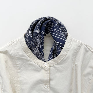 Navy silk scarf with white paisley pattern styled as a neckerchief on a crisp white button-up shirt, showcasing the hand-rolled edges and elegant design.