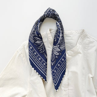 Navy silk scarf with white paisley pattern and striped edges, styled as a neckerchief on a crisp white shirt against minimal background.