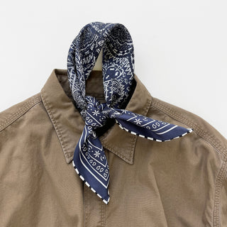 Navy silk scarf with white paisley pattern tied elegantly at the collar of a khaki shirt, featuring hand-rolled edges and traditional bandana design