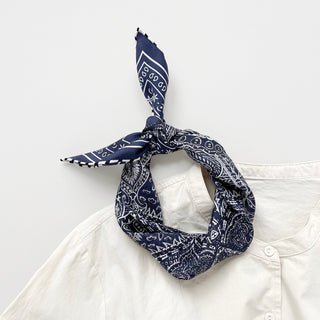 Navy blue silk scarf with white paisley pattern tied in bandana style, displayed on collar of white shirt, showing hand-rolled edges