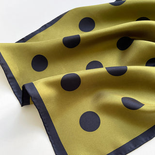 Olive green silk scarf with navy blue polka dots and hand-rolled edges, showing lustrous fabric texture and classic pattern design