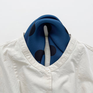 Yale blue silk scarf with large black polka dots styled as a neckerchief with a white button-up shirt, showcasing elegant hand-rolled edges