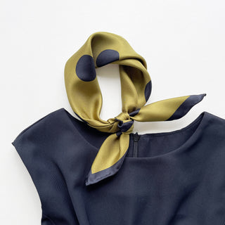 Olive green silk scarf with navy polka dots tied elegantly around collar of navy blouse, showcasing luxurious twill texture and hand-rolled edges