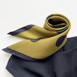 Olive green silk scarf with navy blue polka dots and border, elegantly rolled to display its smooth texture and hand-rolled edges