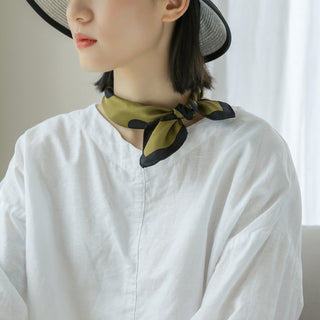 Olive green silk neckerchief with black polka dots tied elegantly around neck, styled with white linen shirt and straw hat