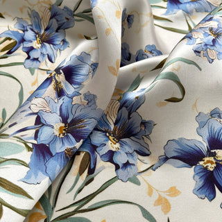Luxurious silk scarf with delicate blue bell flowers pattern, displaying elegant folds on cream background with green stems and subtle gold accents.