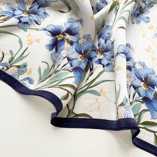 Luxurious silk scarf with delicate blue bell flower pattern on white background, featuring navy blue trim and soft green foliage accents.