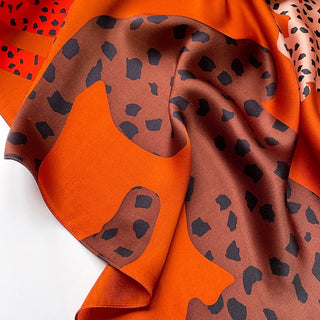 Burnt orange silk scarf with brown leopard print pattern, elegantly draped to showcase its smooth texture and vibrant colors