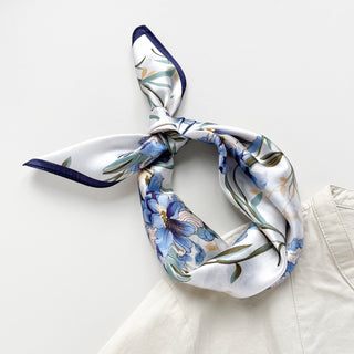 Silk bandana scarf with blue bell floral pattern on white background, featuring navy trim and delicate botanical design, elegantly tied in knot