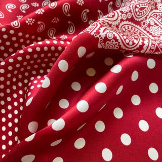 Luxurious red silk scarf with white paisley patterns and polka dots of varying sizes, showcasing the fabric's smooth texture and elegant design.