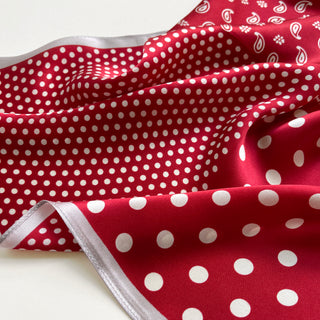 Red silk bandana with white polka dots and paisley pattern, featuring a silver edge trim. The silky fabric shows elegant folds revealing its lightweight texture.