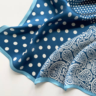 Blue silk bandana scarf with white polka dots and paisley pattern, featuring light blue trim edge, displayed in gentle folds showing texture