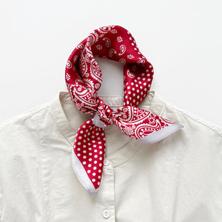 Red silk bandana scarf with white paisley and polka dot patterns tied around collar of cream shirt, showcasing versatile styling