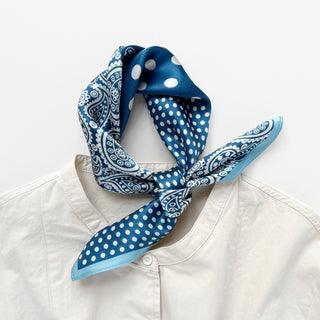 Blue silk bandana scarf with white paisley and polka dot patterns, tied stylishly around a white shirt collar