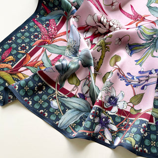 Luxurious pink silk bandana scarf featuring botanical floral pattern with vibrant tropical flowers, dark green leaves and navy border with geometric design