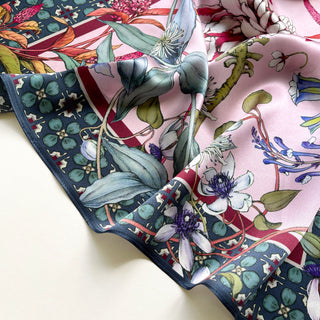 Pink silk bandana scarf with detailed botanical floral print featuring vibrant flowers, green leaves, and navy blue border with decorative pattern