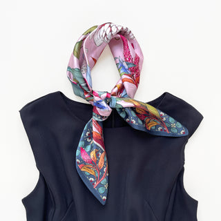 Pink silk bandana scarf with vibrant botanical print featuring pink, blue, and green florals, tied elegantly around a navy top neckline