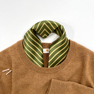 Moss green silk bandana with gold diagonal stripes styled as a neckerchief on a camel cashmere sweater, showcasing luxurious texture and pattern