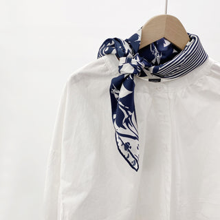 Navy and white silk square scarf styled as a neckerchief on white shirt, featuring mixed patterns of floral motifs and stripes