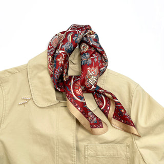 Red silk scarf with vintage floral pattern and gold border elegantly draped around beige jacket collar, displaying intricate blue and cream details