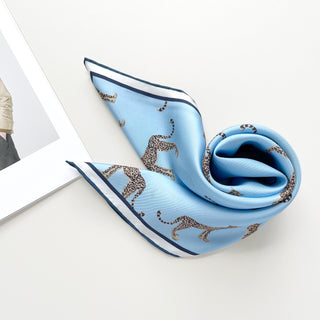 Sky blue silk scarf with leopard print pattern and navy border, elegantly draped to display its luxurious texture and hand-rolled edges