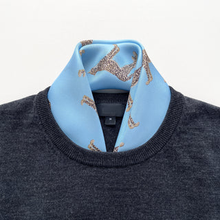 Sky blue silk neckerchief with leopard print pattern styled with a dark gray sweater, showcasing the luxurious hand-rolled silk twill texture