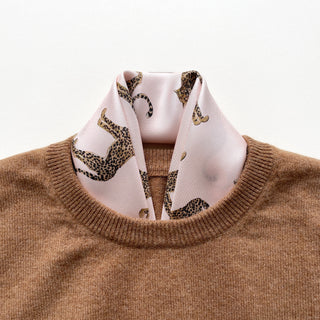Pink silk neckerchief with leopard print pattern styled inside a camel-colored sweater neckline, showcasing the luxurious silk twill texture.
