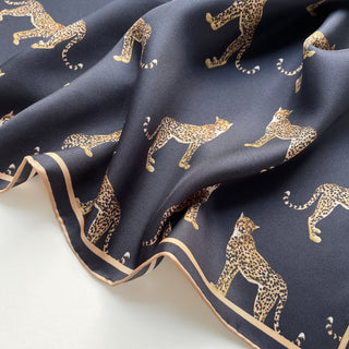 Black silk scarf with gold leopard print pattern and beige hand-rolled edge, showcasing luxurious twill texture in elegant folds