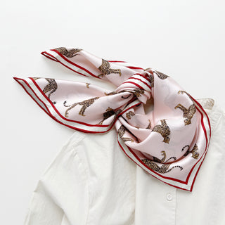 Pink silk scarf with leopard print pattern and red border, elegantly styled over a white shirt collar showing luxurious hand-rolled edges