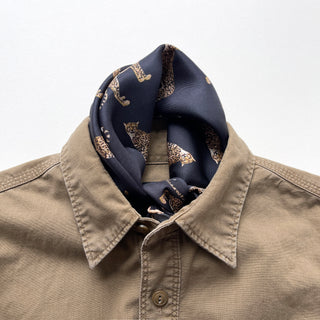 Navy blue silk neckerchief with leopard print pattern elegantly styled with beige button-up shirt, showcasing luxurious hand-rolled silk twill