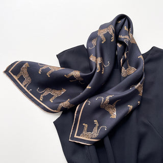 Black silk scarf with gold leopard print pattern throughout and elegant beige border, elegantly draped to display luxurious silk twill texture
