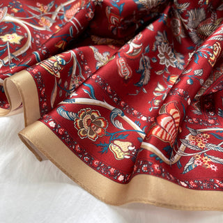 Rich red silk scarf with vintage floral pattern featuring blue, gold and cream details, edged with elegant gold trim, displaying luxurious sheen