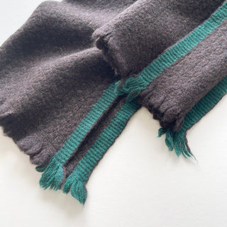 Detail of the teal green contrast edging and short fringed ends on a dark chocolate brown cashmere scarf.