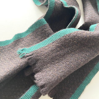 Detail of the teal green contrast edging and short fringed ends on a dark chocolate brown cashmere scarf.