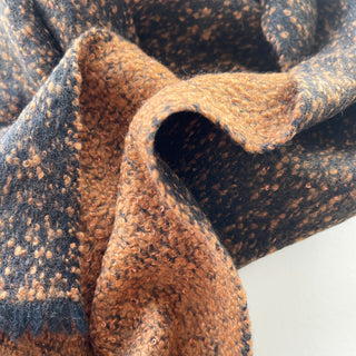 Close-up of the soft black and warm brown flecked texture of a 100% cashmere scarf.
