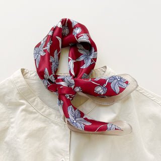 Red silk bandana scarf with blue-outlined floral pattern tied elegantly around collar of cream blouse, showcasing versatile styling
