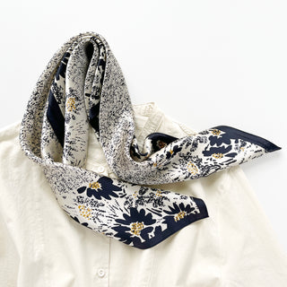 Beige silk scarf with navy floral pattern and gold accents draped elegantly over white shirt, showing luxurious texture and delicate design