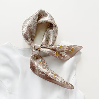 Beige silk bandana scarf with delicate floral pattern featuring brown flowers with gold centers, elegantly knotted on white fabric