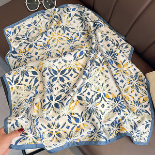 Square silk bandana scarf with dusty blue border and cream background featuring artistic floral pattern in blue and yellow