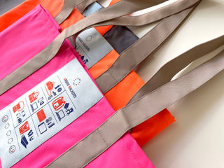 Recycled large tote bags in vibrant pink and orange colors with beige handles, featuring Urban Walkers labels and product icons, made from eco-friendly RPET material.